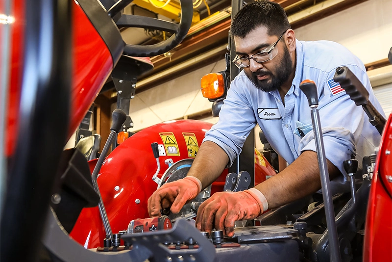 Buening Implement service technician performing routine maintenance on a Massey Ferguson compact tractor.